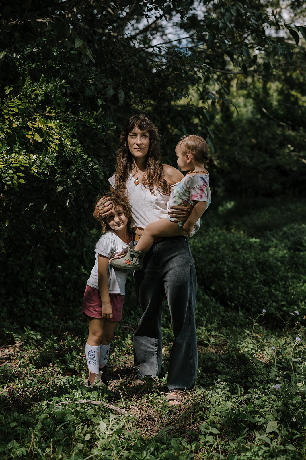Chrissy Beth standing with both of her children in a sunlit green garden.